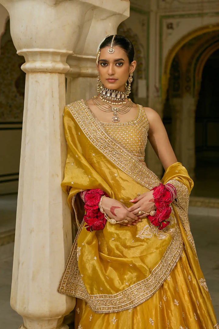 Woman in traditional yellow lehenga with gold jewelry and red flowers in a decorative setting