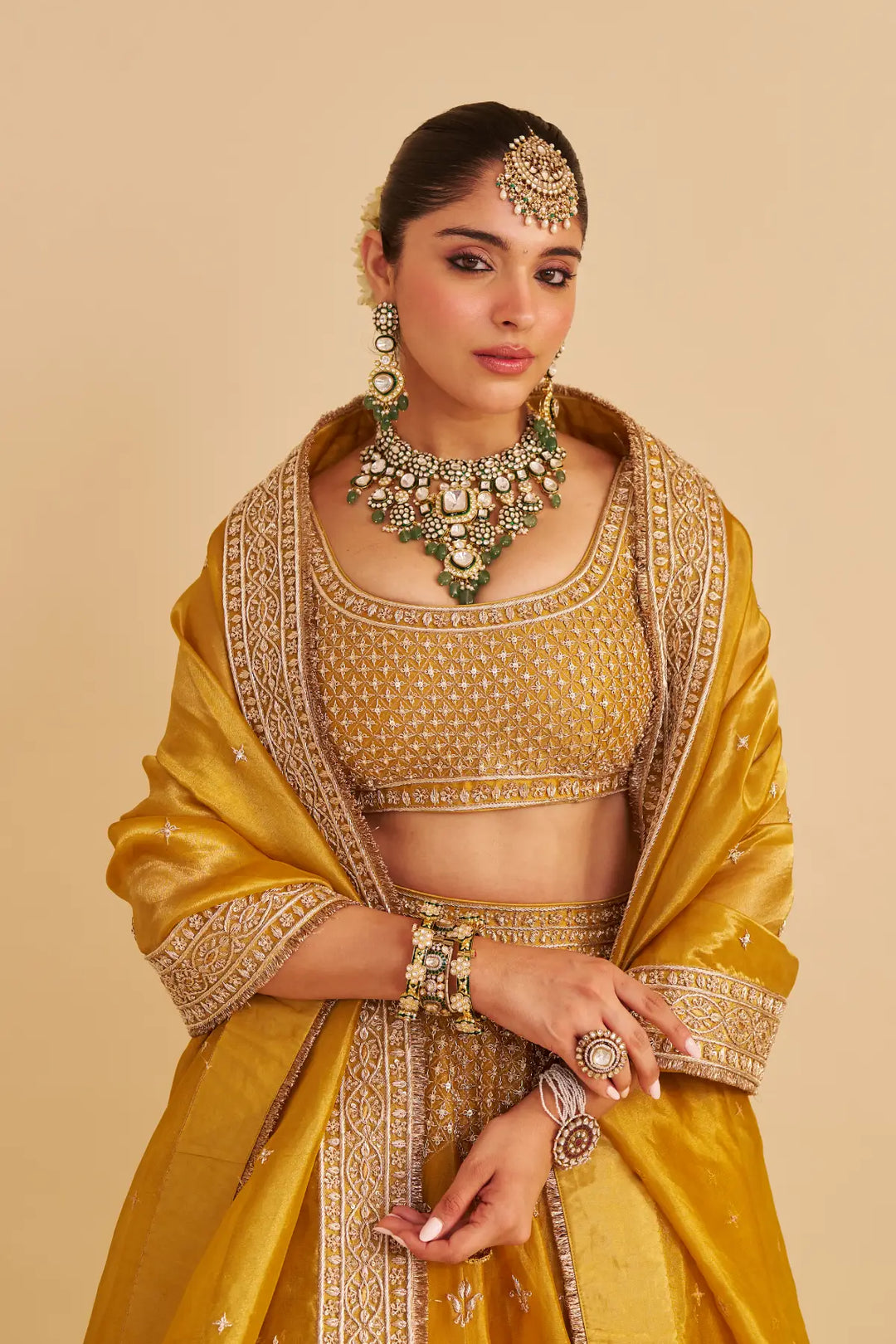 Woman in a traditional yellow lehenga with intricate embroidery and jewellery against a beige background