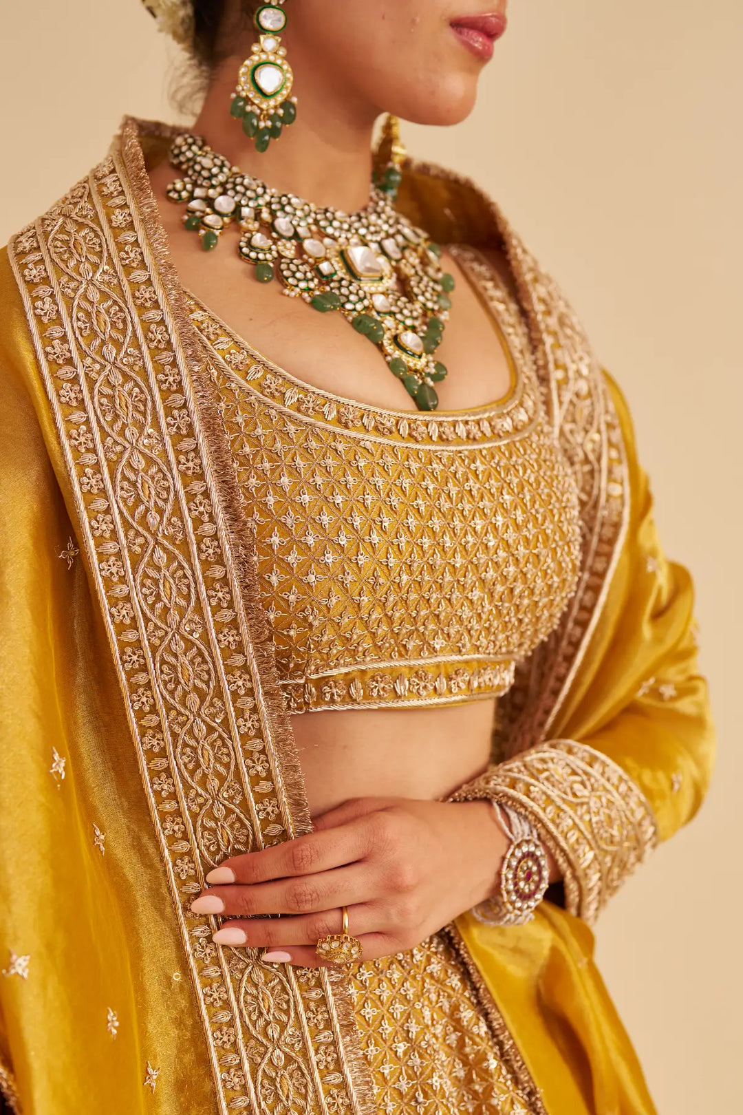 Close-up of a person wearing a yellow embroidered saree with gold jewelry on a beige background