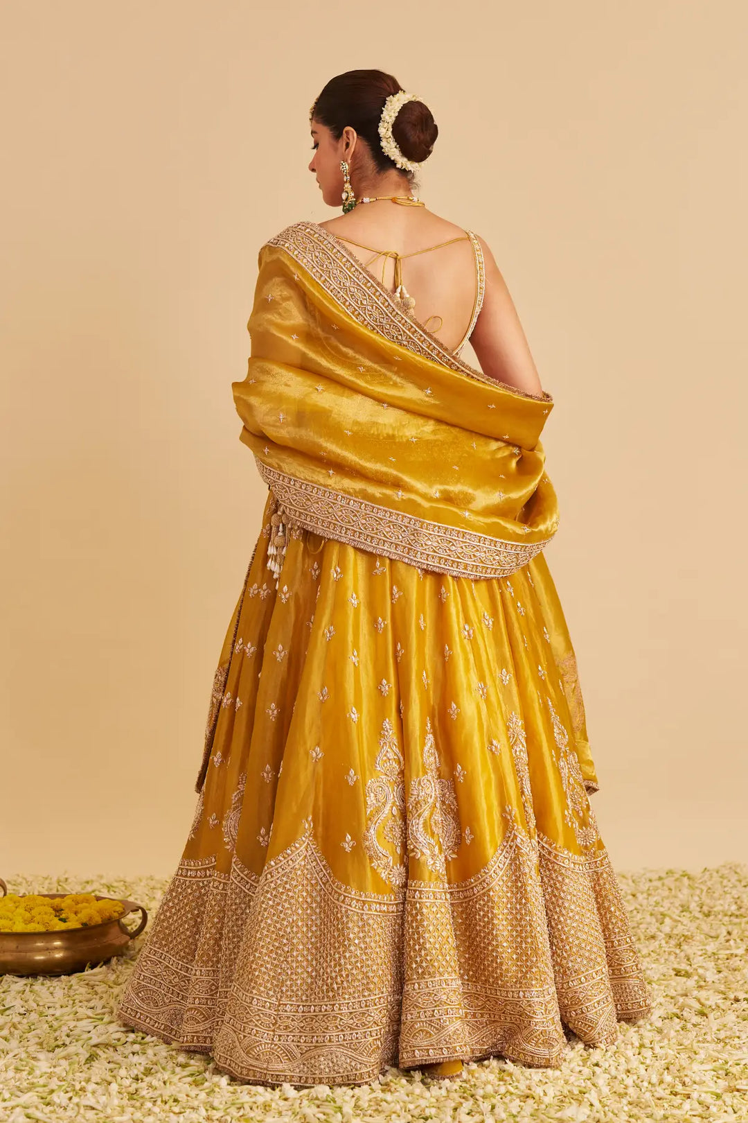 Woman wearing a yellow lehenga with gold details on a beige background