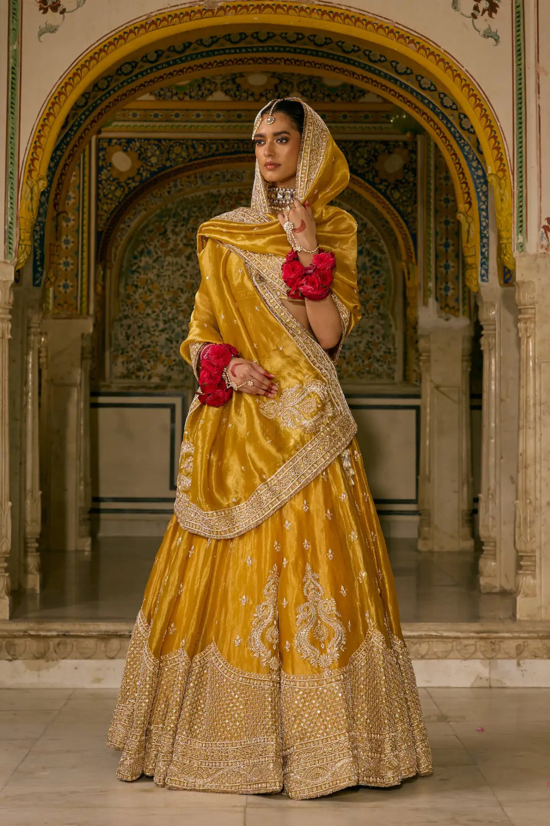 Woman in a yellow and gold traditional lehenga standing in an ornate architectural setting.