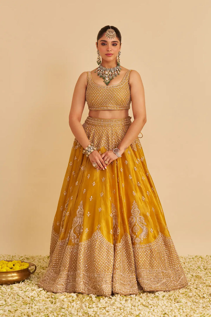 Woman in a traditional mustard yellow and gold lehenga with jewelry on a beige background