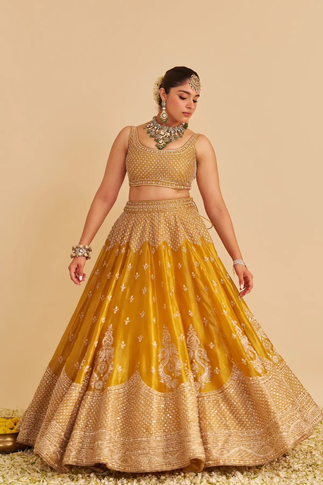 Woman wearing a traditional yellow and gold outfit with jewelry on a beige background