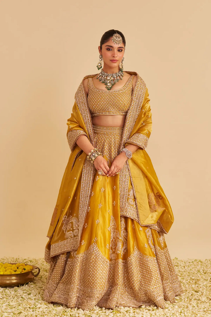 Woman in a traditional yellow and gold lehenga with jewellery against a beige background