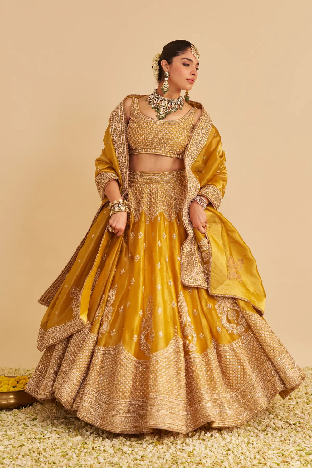 Woman in a traditional yellow and gold lehenga with jewellery against a beige background