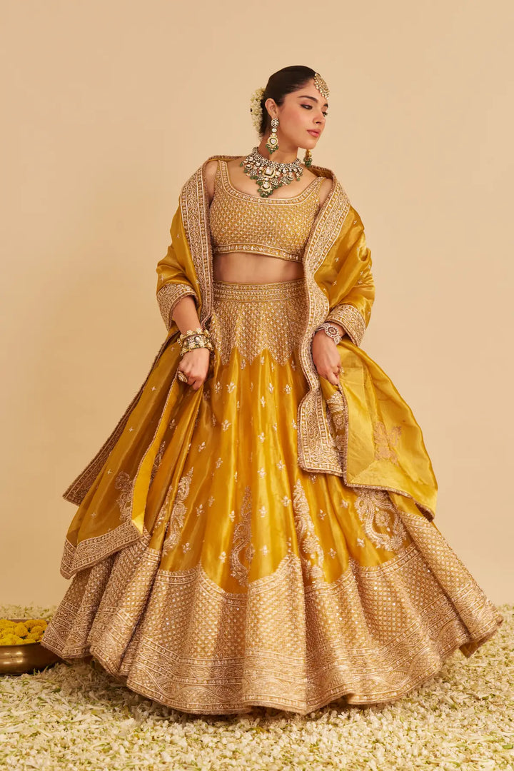 Woman in a traditional yellow and gold lehenga with jewellery against a beige background