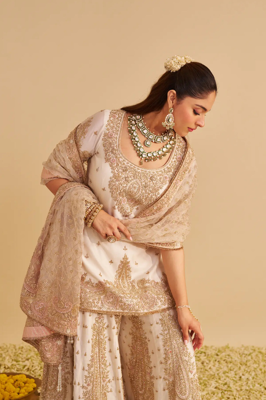 Woman in traditional embroidered Sharara with jewellery against a beige background