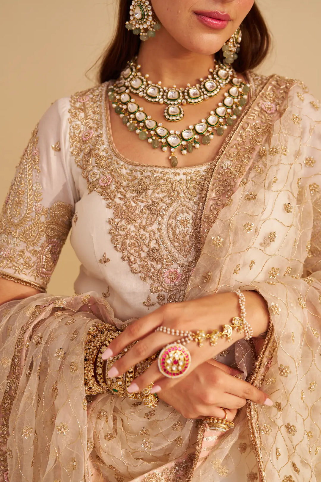 Close-up of a person wearing traditional embroidered Sharara with jewellery on a beige background