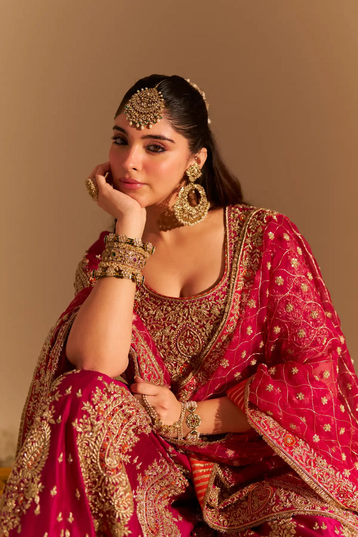 Woman in traditional pink and gold embroidered Sharara with jewellery against a beige background