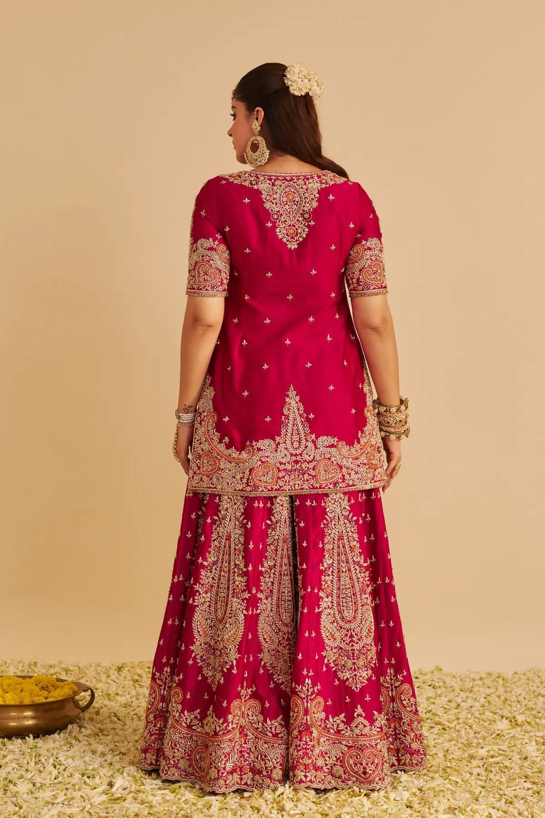 Woman wearing a red embroidered traditional Sharara on a beige background