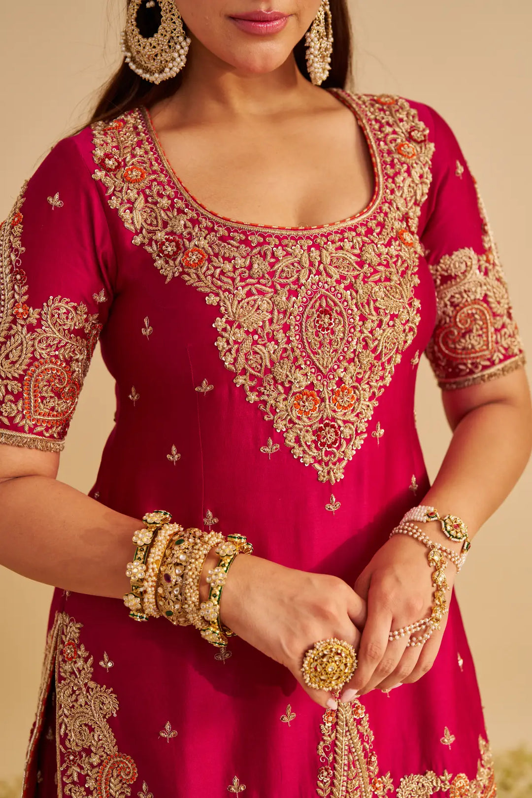 Red traditional Sharara with gold embroidery and jewellery on a beige background