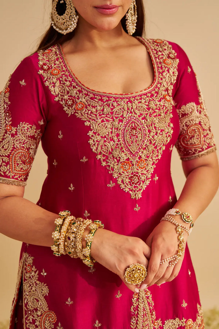 Red traditional Sharara with gold embroidery and jewellery on a beige background