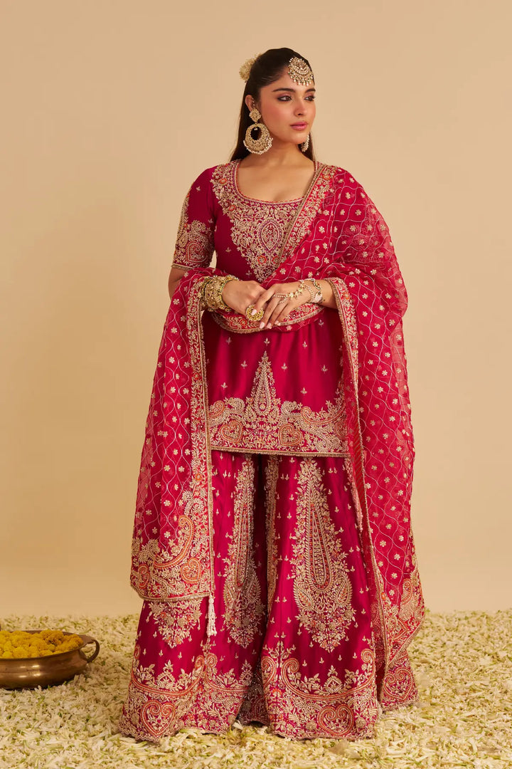 Woman in a traditional red and gold embroidered Sharara on a beige background