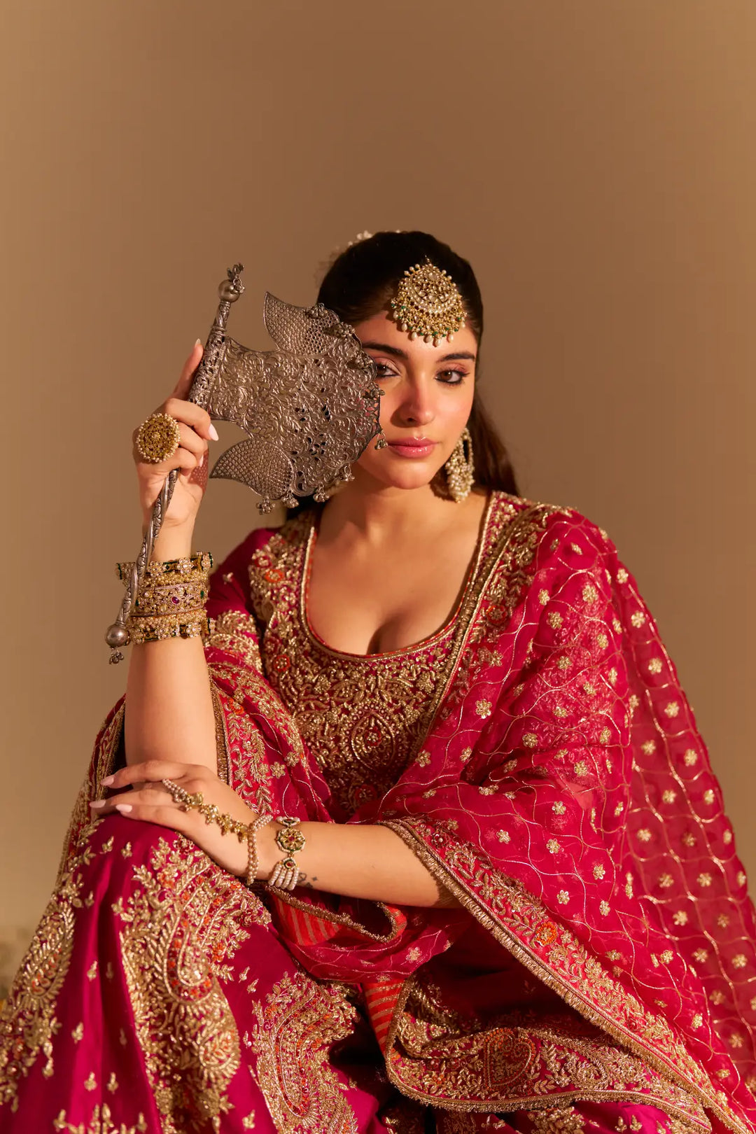 Woman in traditional pink and gold saree with jewelry against a beige background