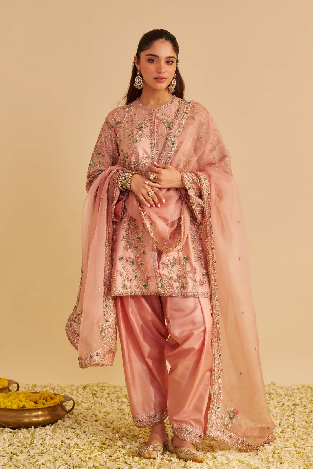 Woman wearing a traditional pink outfit with intricate patterns on a beige background