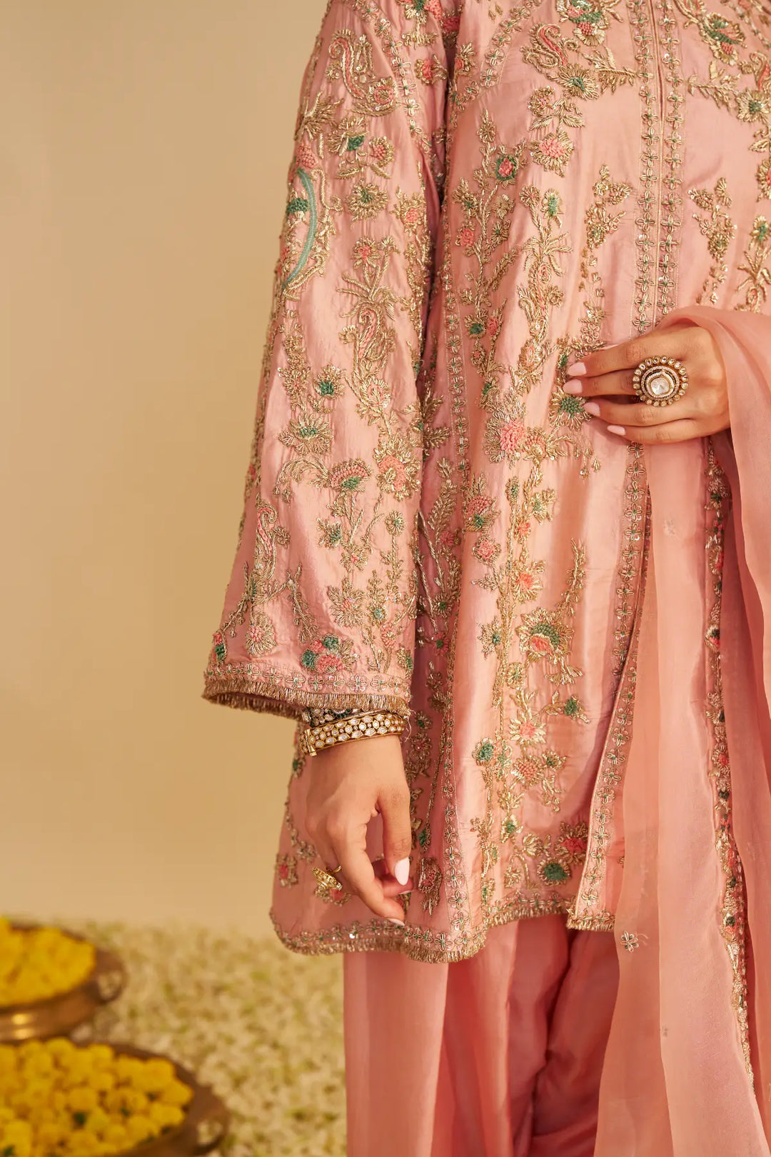 Person wearing a pink embroidered traditional outfit with a beige background