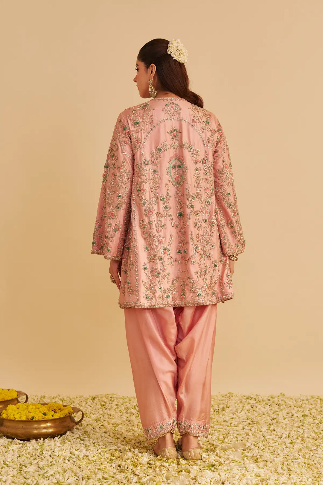 Woman wearing a traditional pink embroidered outfit with a beige background
