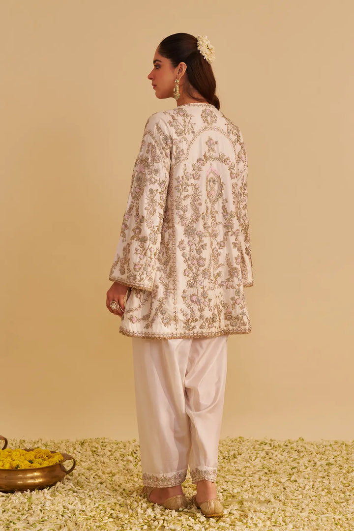 Woman wearing a floral embroidered kurta with white pants on a beige background