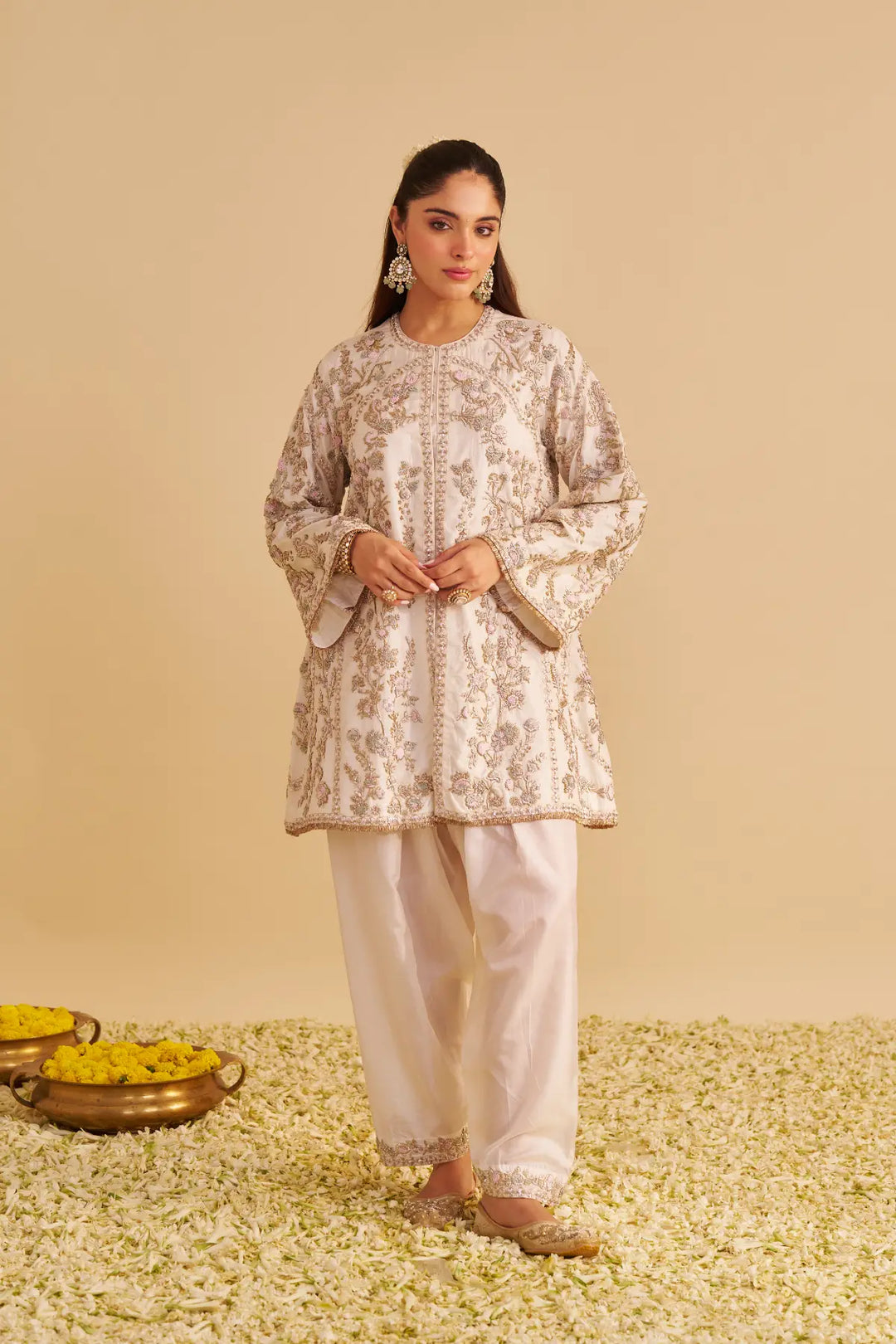 Woman wearing a patterned top and white pants standing on a textured surface with a beige background