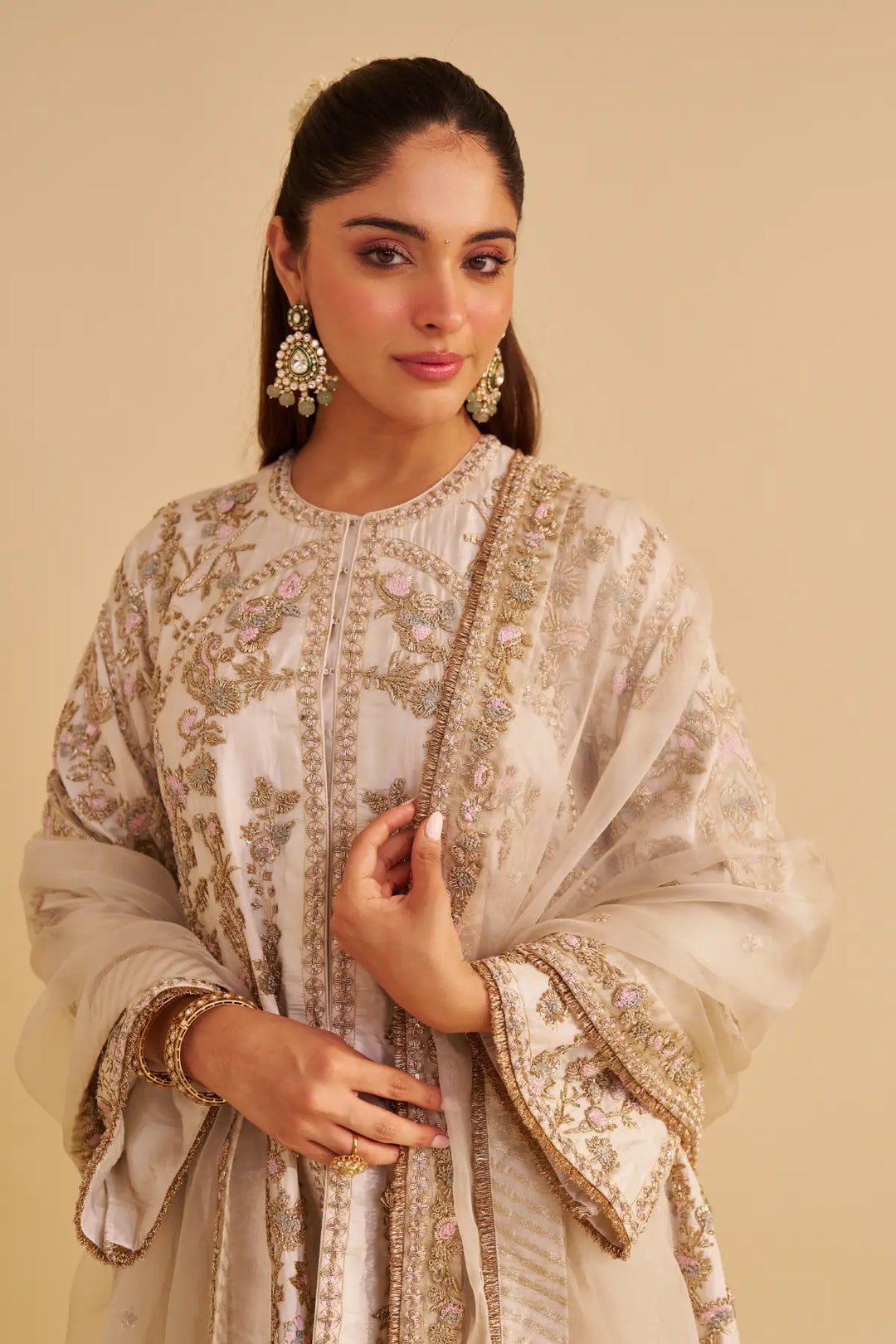 Woman wearing a beige embroidered traditional outfit with a plain background