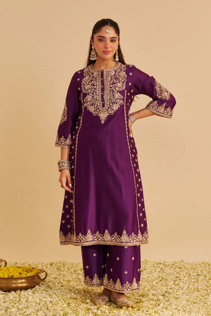 Woman wearing a purple traditional Kurta with gold embroidery on a beige background