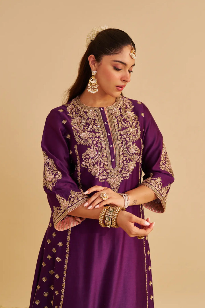 Woman wearing a purple embroidered traditional Kurta on a beige background