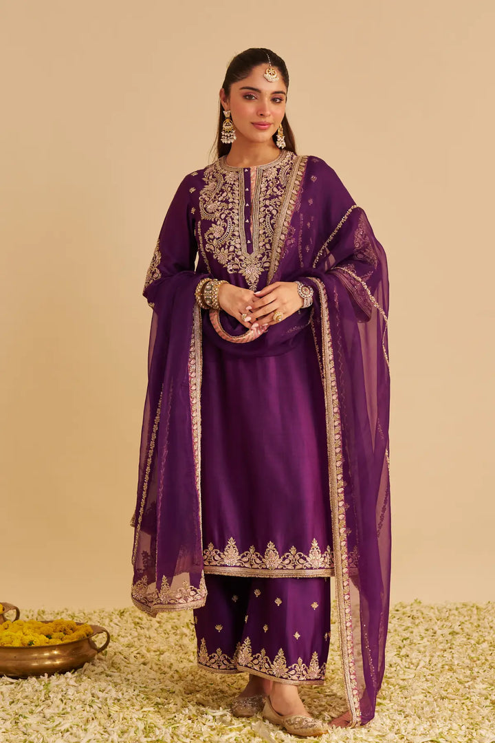 Woman in a traditional purple Kurta with gold embroidery on a beige background