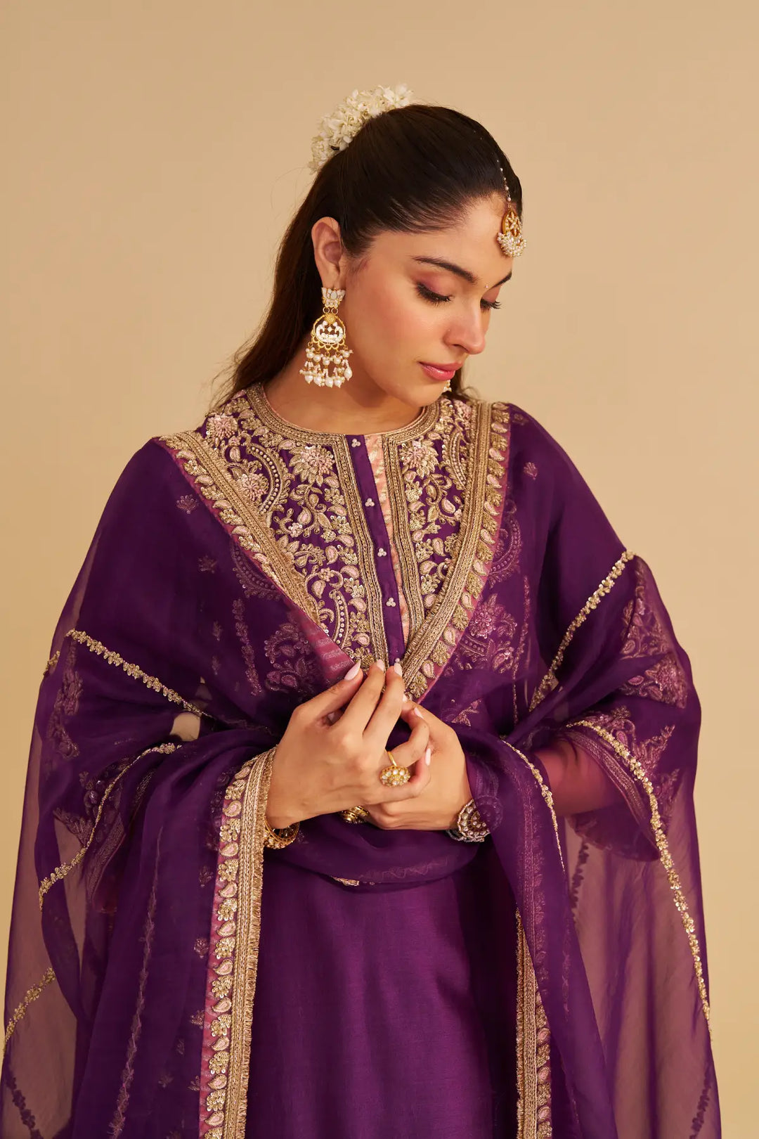 Woman wearing a purple traditional Kurta with gold embroidery on a beige background