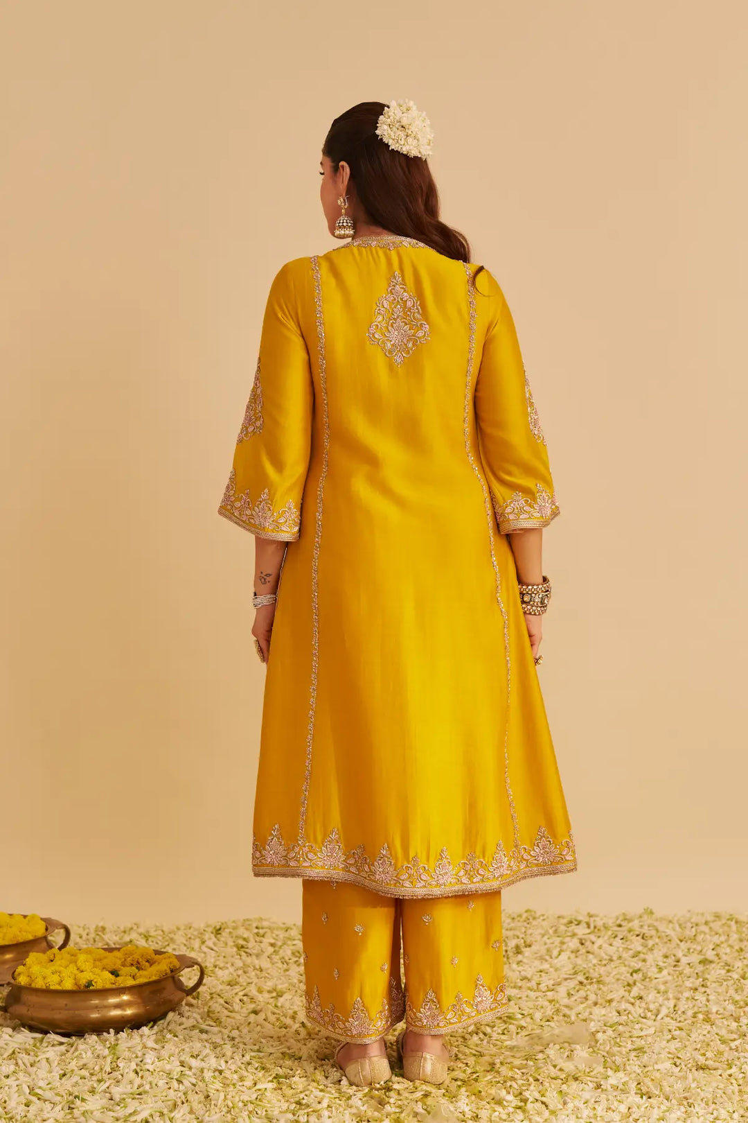 Woman wearing a yellow traditional outfit with intricate designs on a beige background
