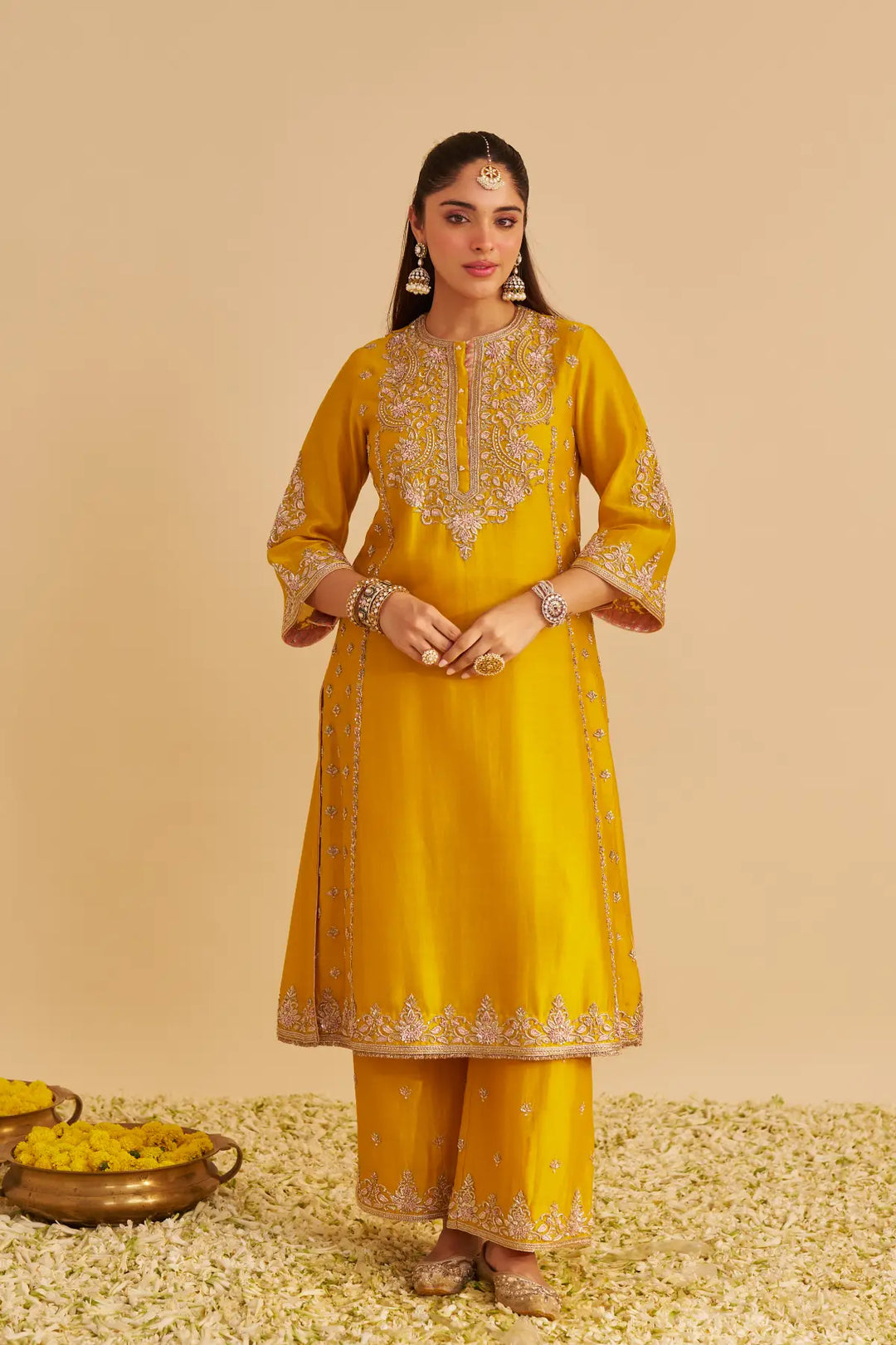 Woman wearing a yellow traditional Kurta with intricate designs on a beige background