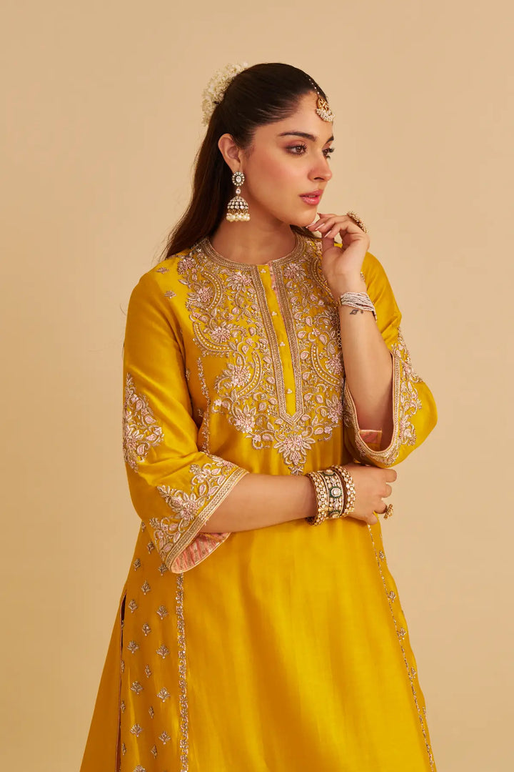 Woman wearing a yellow traditional outfit with intricate designs on a beige background