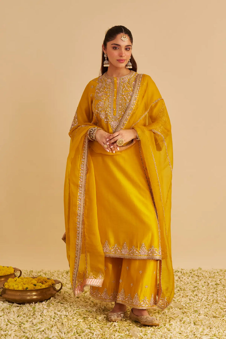 Woman in a yellow traditional outfit with gold embroidery on a beige background