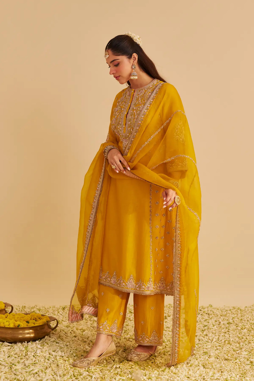 Woman in a yellow traditional outfit with gold embroidery on a beige background