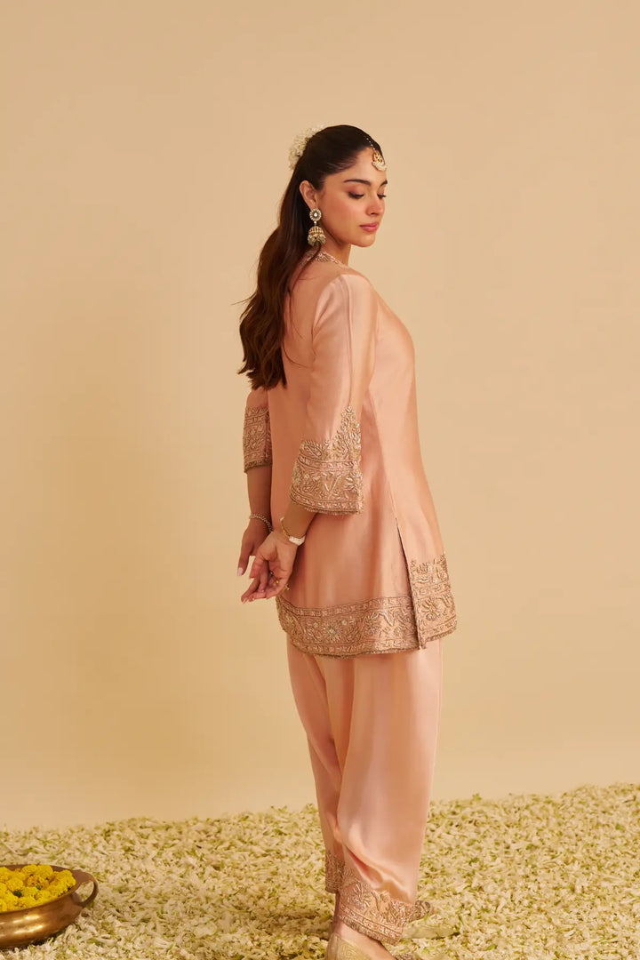 Woman wearing a peach embroidered kurta against a beige background