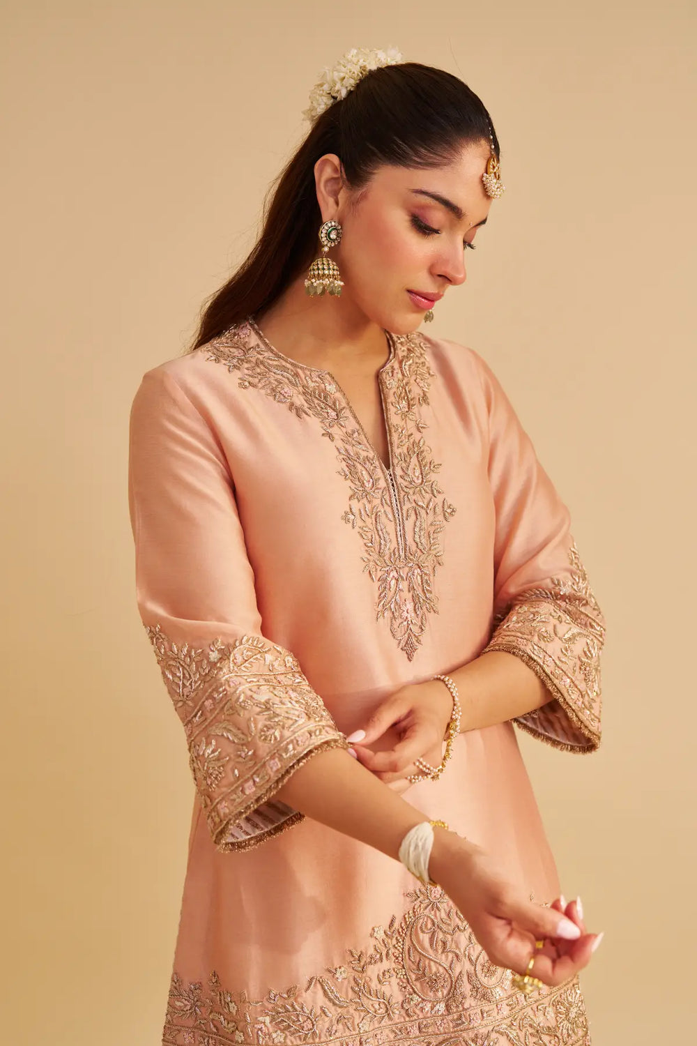 Woman wearing a pink embroidered kurta against a beige background
