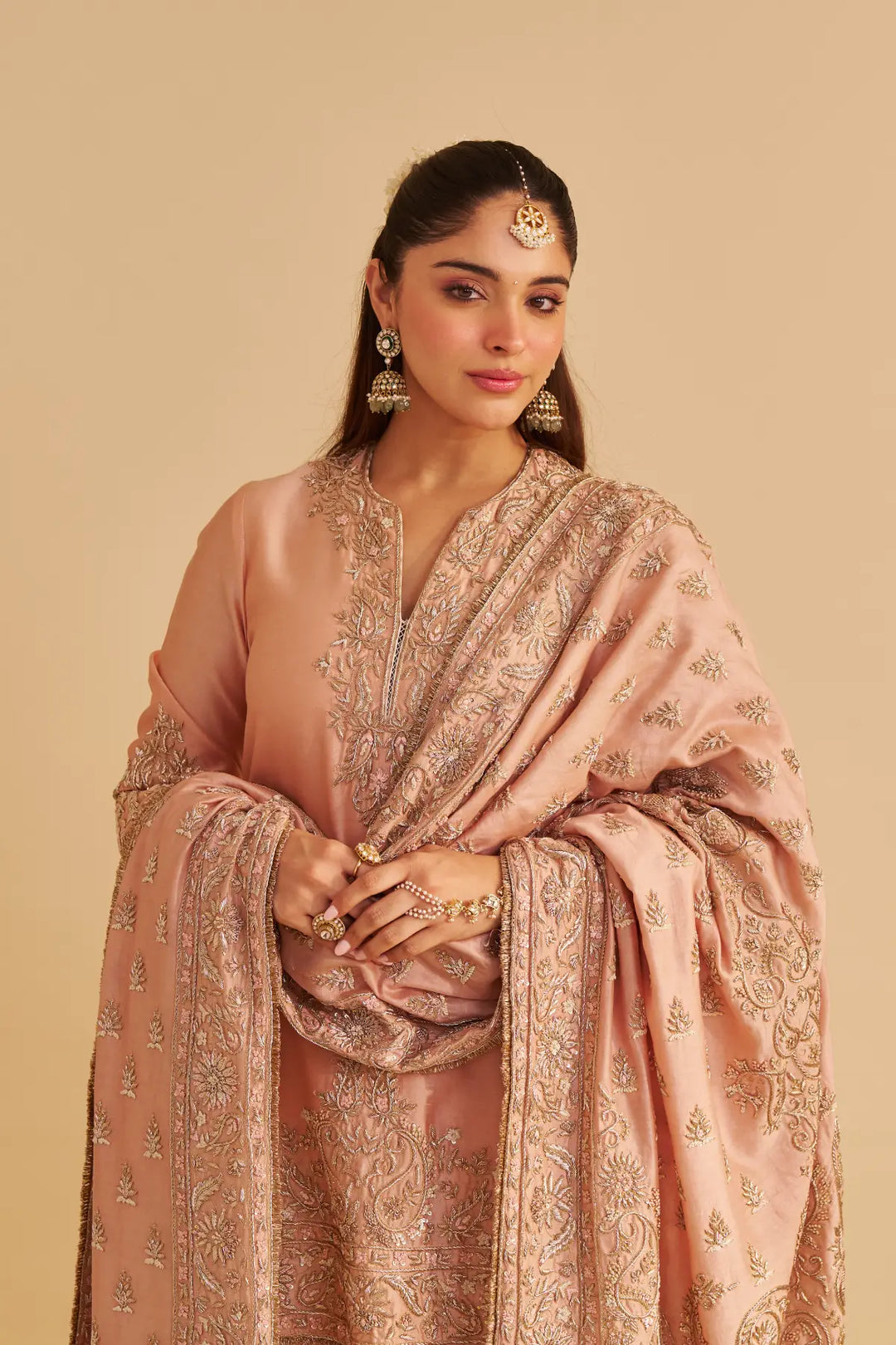 Woman wearing a traditional pink kurta with intricate patterns on a beige background