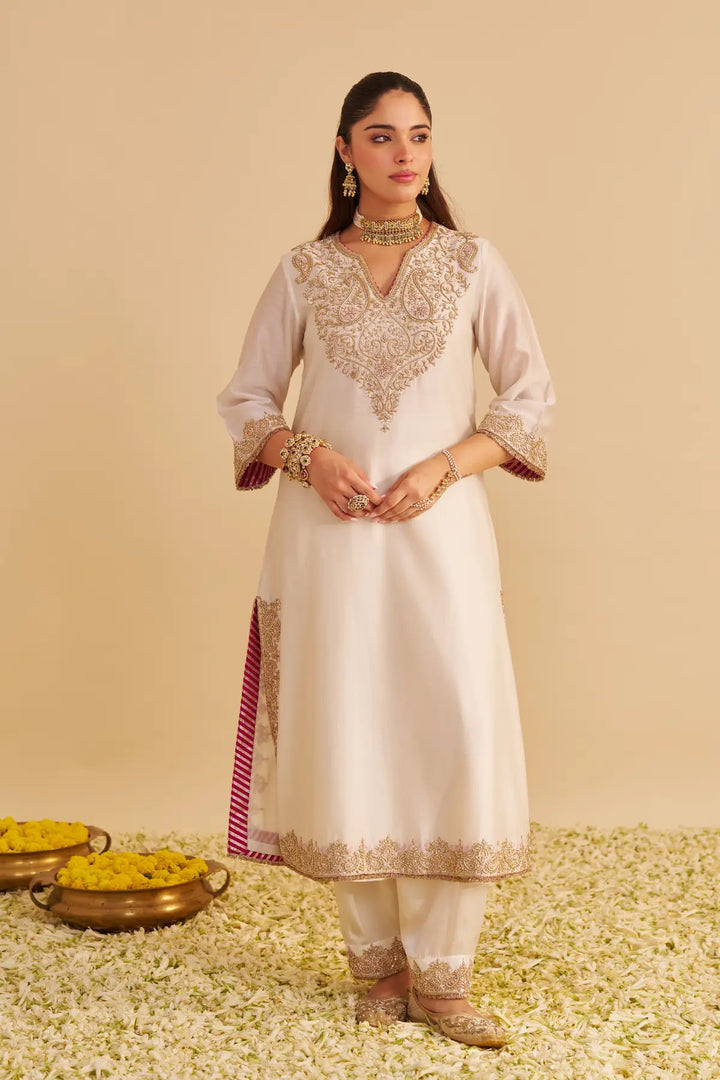 Woman in a white embroidered outfit standing on a textured surface with decorative elements.