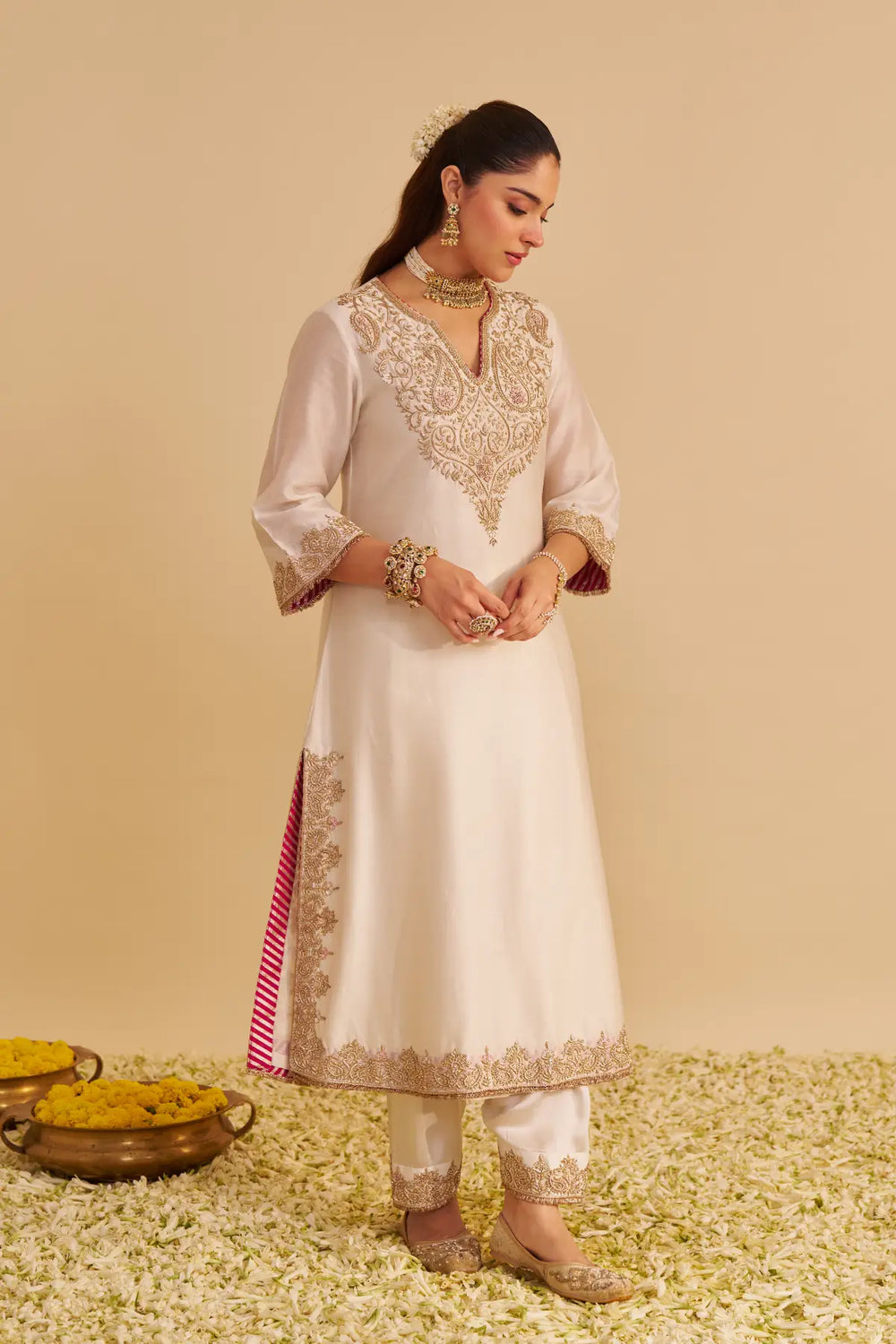 Woman in a white and gold embroidered traditional outfit on a beige background