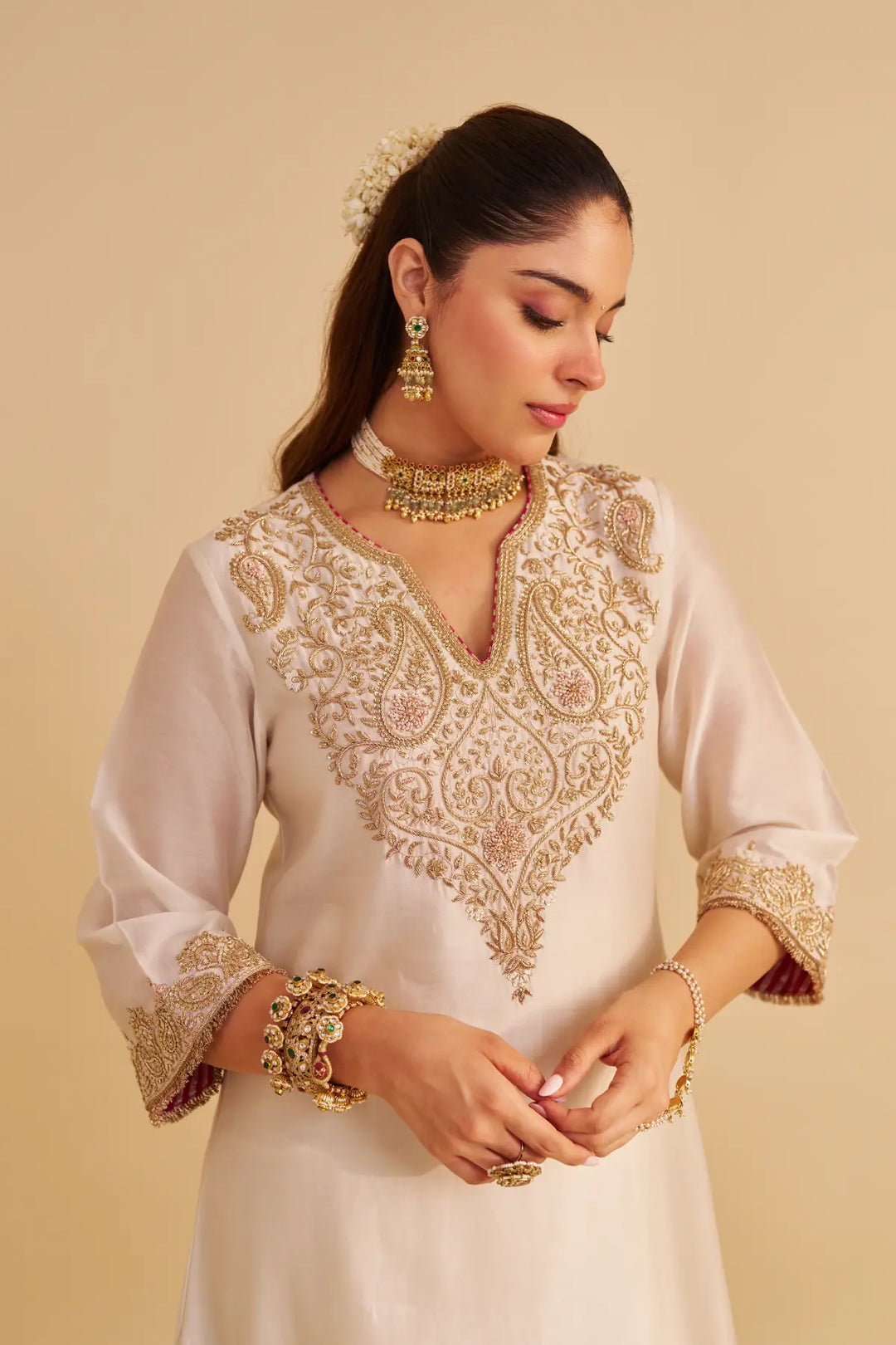Woman wearing a white embroidered kurta with gold details on a beige background