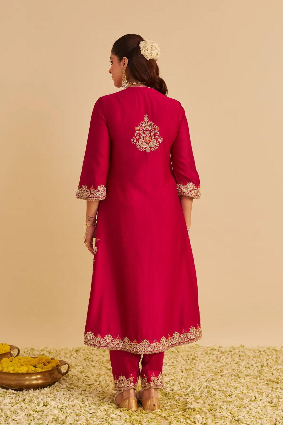 Woman wearing a red traditional outfit with intricate embroidery on a beige background