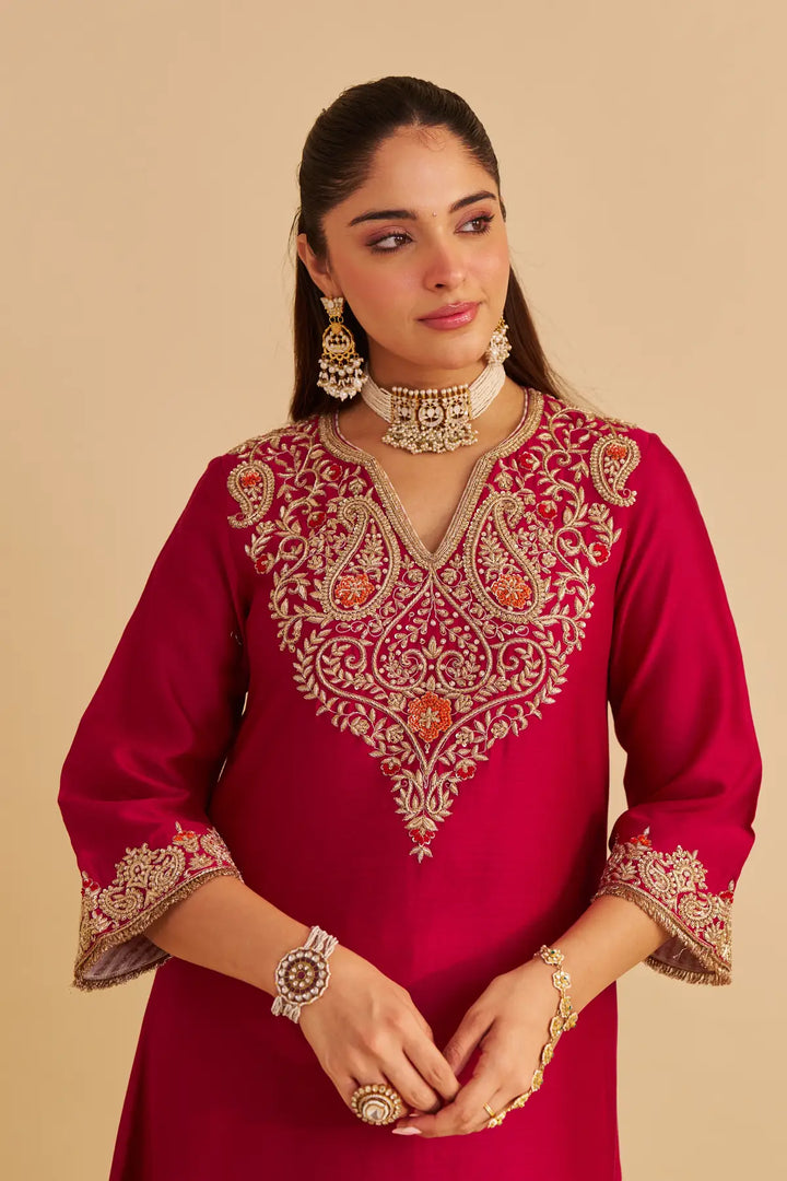 Woman wearing a red embroidered traditional outfit with jewelry on a beige background