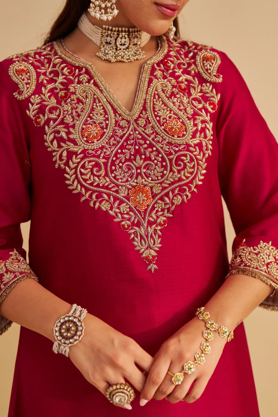 Red embroidered dress with gold detailing worn by a person, against a beige background