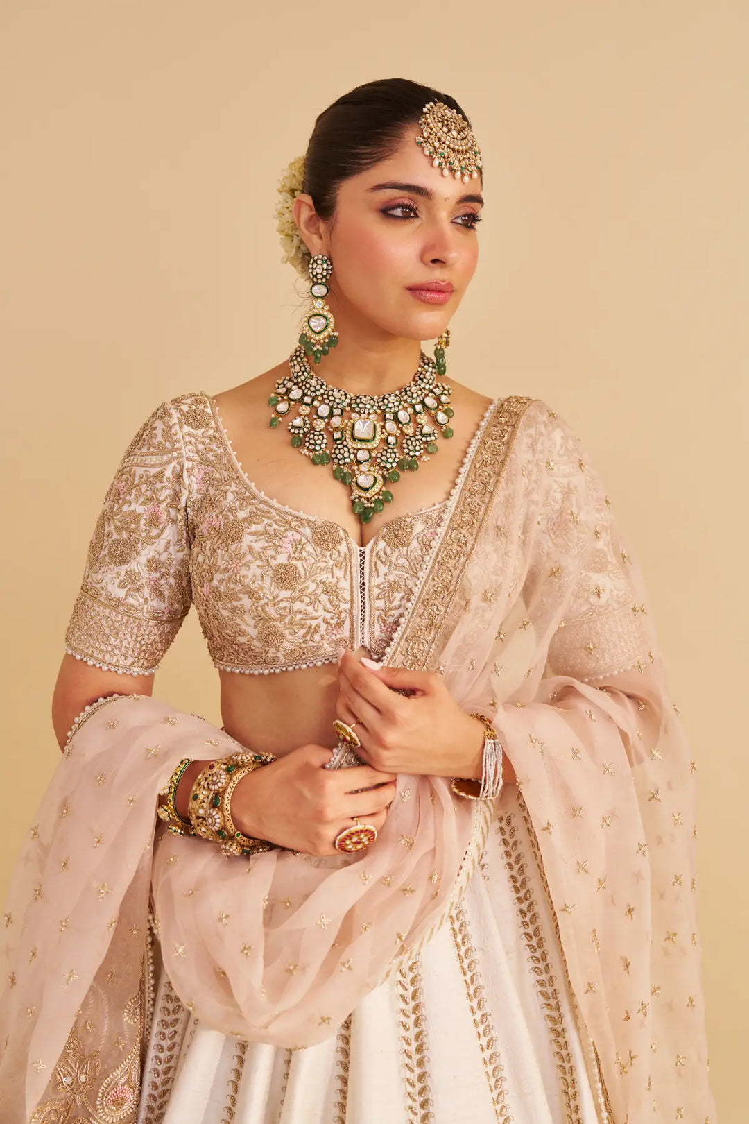Woman in traditional Indian attire with jewelry against a beige background