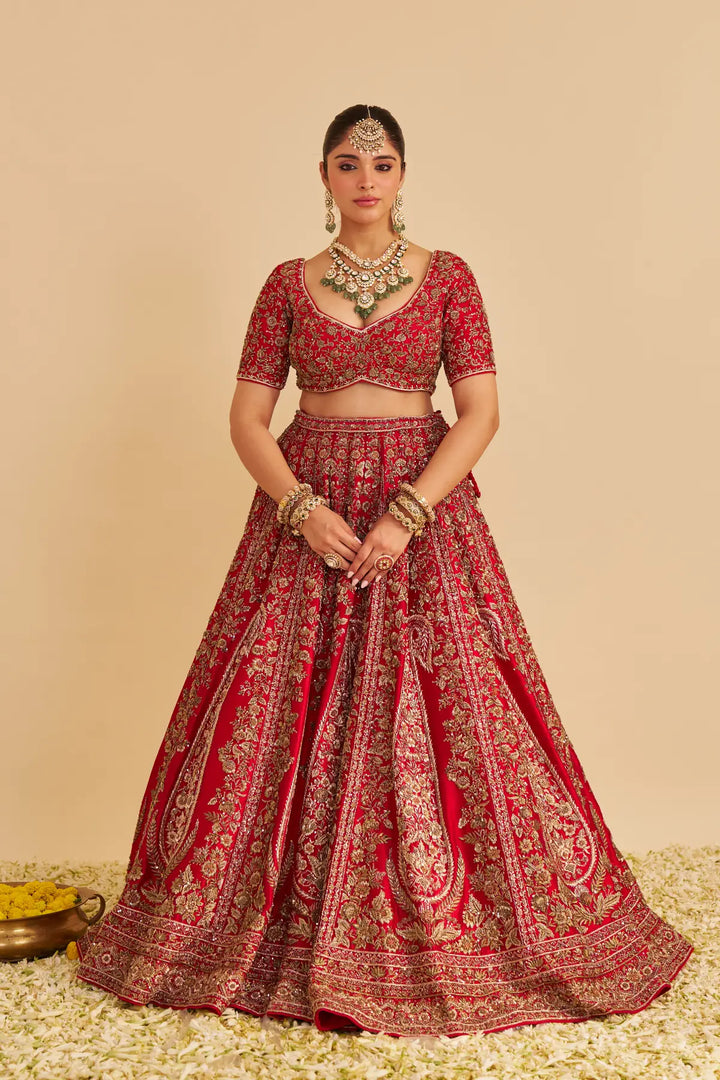Woman wearing a red and gold traditional outfit with jewelry on a beige background