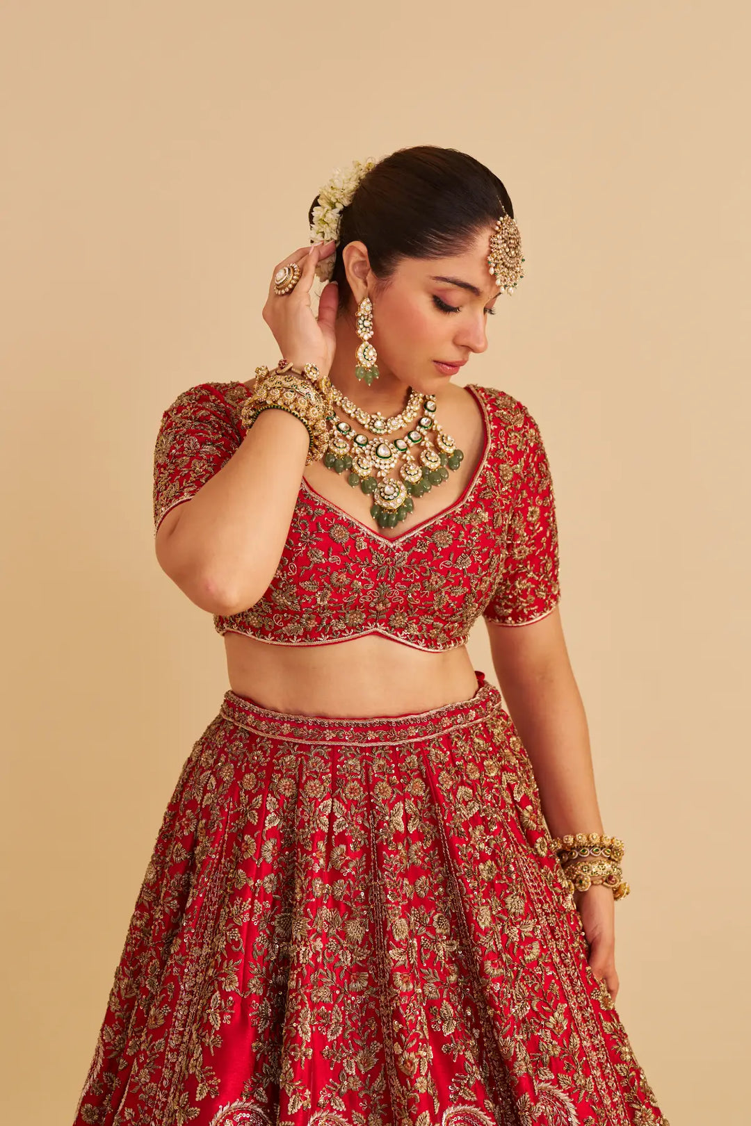 Woman in traditional red and gold embroidered outfit with jewelry on a beige background