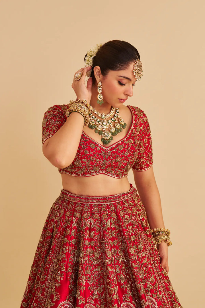 Woman in traditional red and gold embroidered outfit with jewelry on a beige background