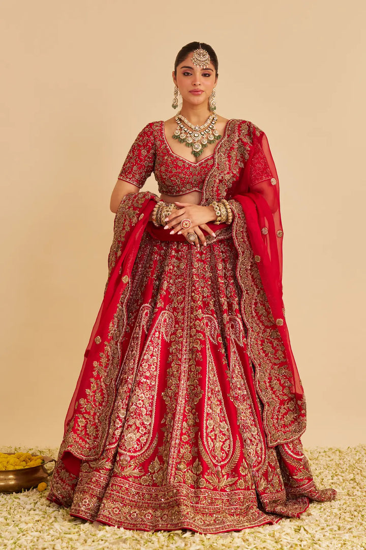 Woman in a red and gold embroidered traditional lehenga with jewellery on a beige background