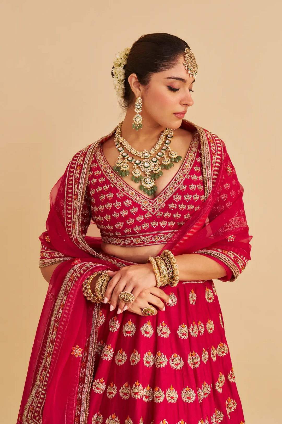 Woman in a red embroidered traditional outfit with gold jewelry on a beige background