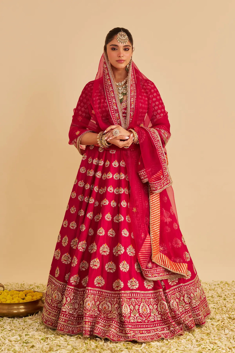 Woman in a traditional red and gold lehenga with jewelry on a beige background