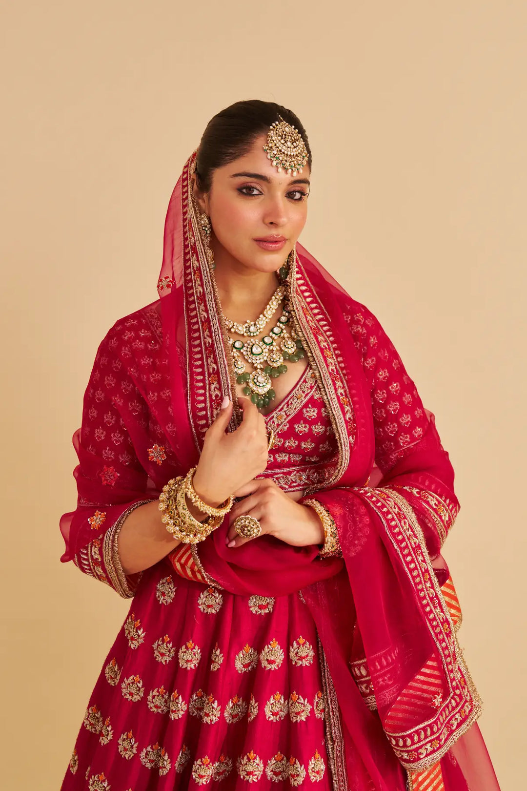 Woman in traditional red and gold embroidered outfit with jewelry on a beige background